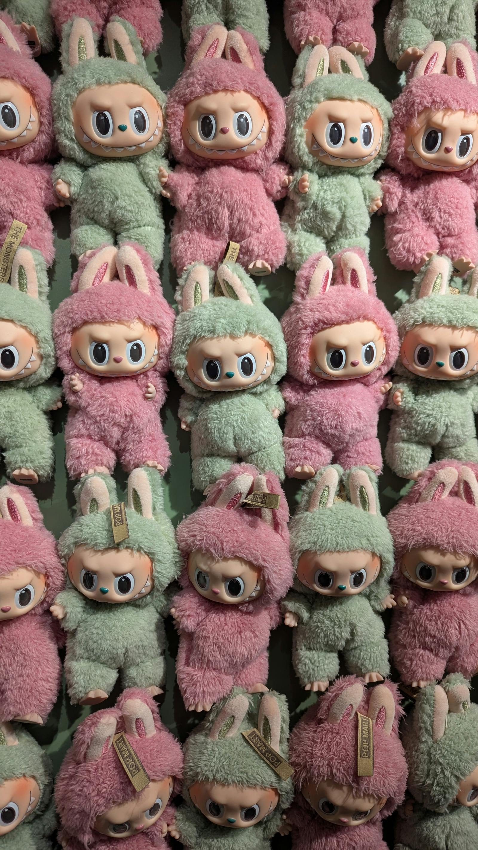 Pared densa de plush toys pastel verdes y rosas con ojos grandes — referencia visual a una colección Squishmallows.